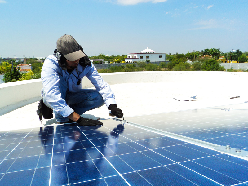 Operario instalando paneles solares sobre la cubierta de un edificio. 