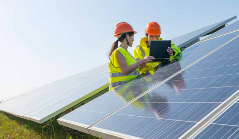 Un hombr y una mujer trabajan junto a un panel fotovoltaico. 