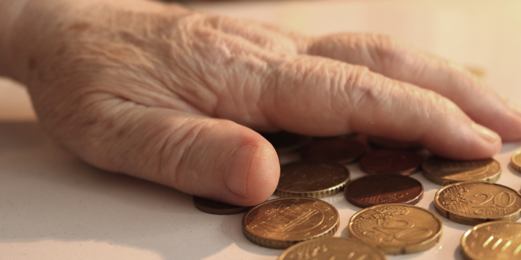 Mano de mujer anciana sobre un montón de monedas de euro. Pobreza energética. Bono social de electricidad. Consumidores vulnerables.