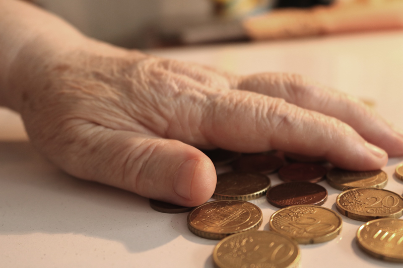 Mano de mujer anciana sobre un montón de monedas de euro. Pobreza energética. Bono social de electricidad. Consumidores vulnerables. 