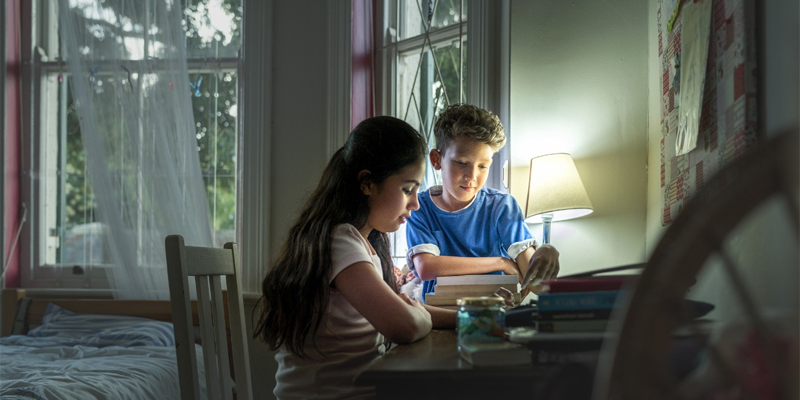 Dos niños estudian en una habitación iluminada por una lámpara. Pobreza Energética.