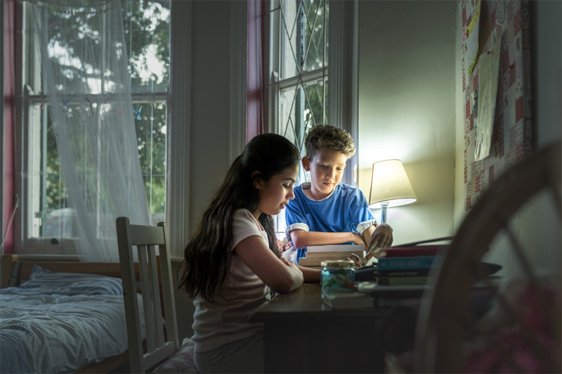 Dos niños estudian en una habitación iluminada por una lámpara. Pobreza Energética. 
