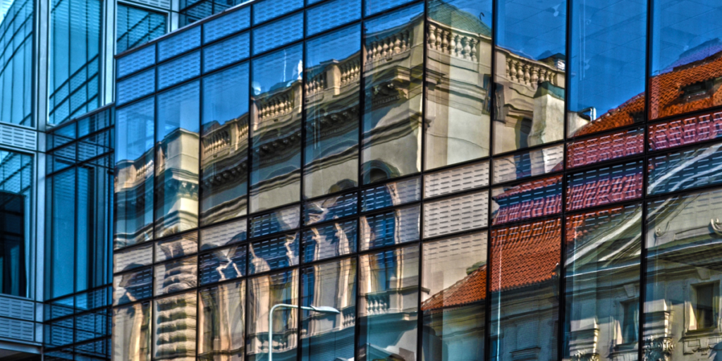 Edificio moderno en cuya fachada se ve reflejada la fachada de un edificio antiguo.