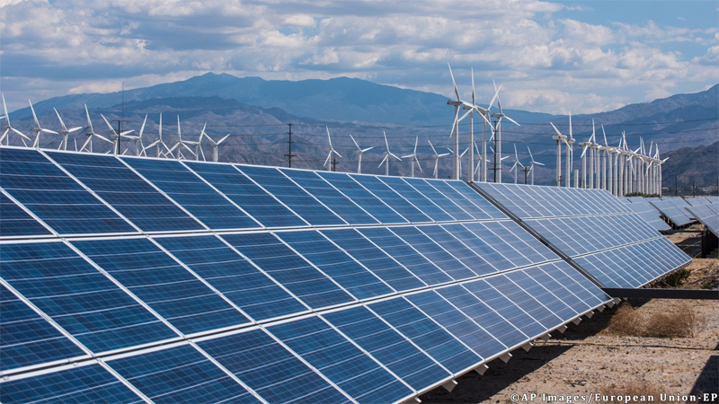 Parque fotovoltaico con un parque eólico al fondo. 