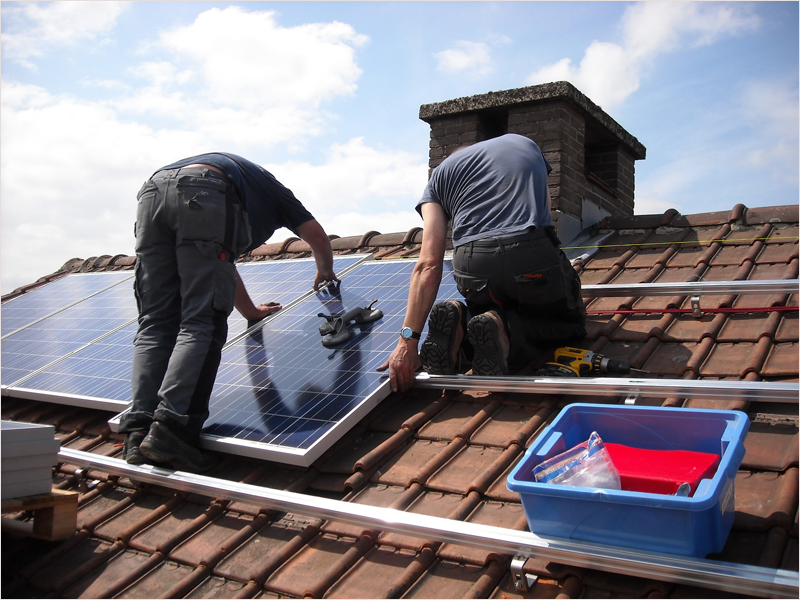 Dos operarios instalan placas solares en en tejado de una vivienda unifamiliar.