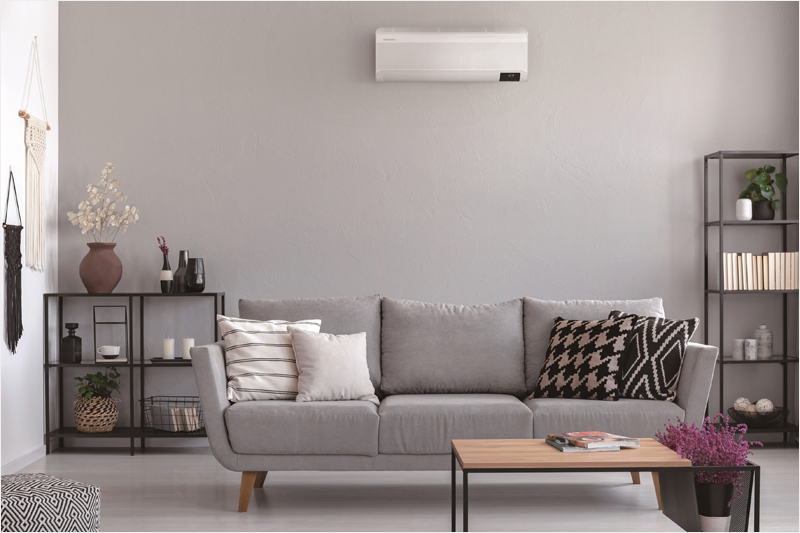 Salón con un sofá, una mesa y muebles y en la pared colgado un climatizador de Samsung con tecnología WindFree.