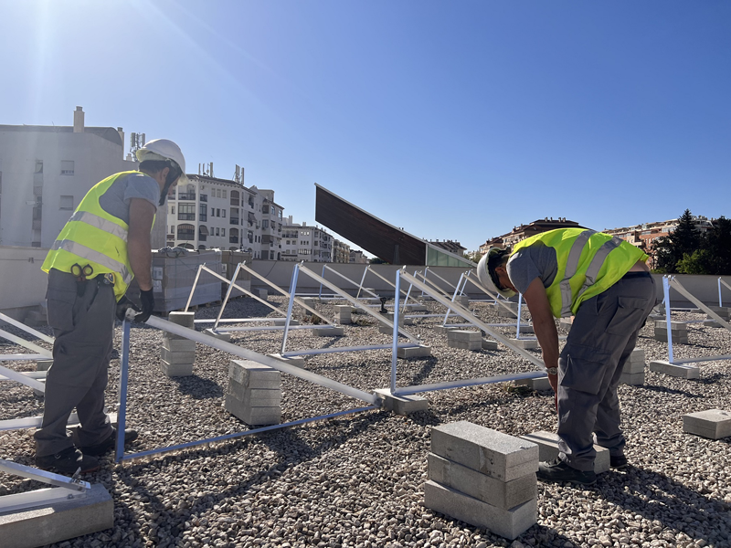 Dos operarios instalan paneles fotovoltaicos en el techo del edificio de FTV.