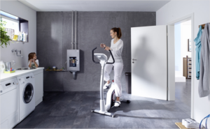 Una madre y una hija en la cocina. La madre haciendo deporte en una bici estática y detras un producto de Resideo.