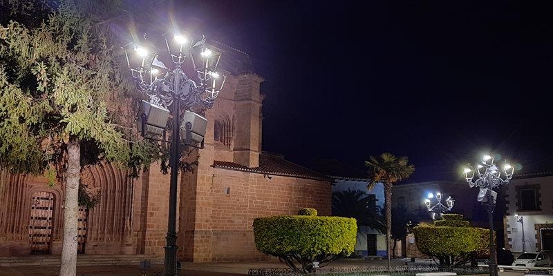 Una calle de noche y una iglesia y delante dos farolas iluminando la noche.