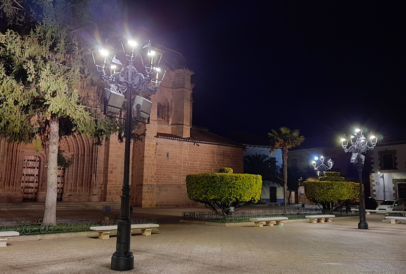 Una calle de noche y una iglesia y delante dos farolas iluminando la noche.