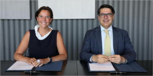 Una mesa grande y un hombre y una mujer sentados en una silla para firmar unos documentos.