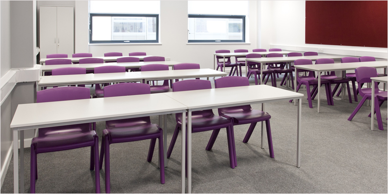 Aula sin alumnos con mesas blancas y sillas moradas.