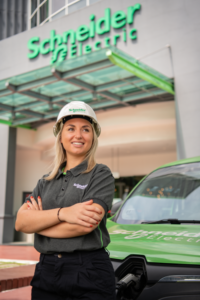 Chica con un gorro de obra delante de una empresa de Schneider Electric.