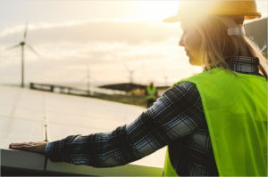 Chica con un gorro de obra en primer plano y al fondo un molino eólico.