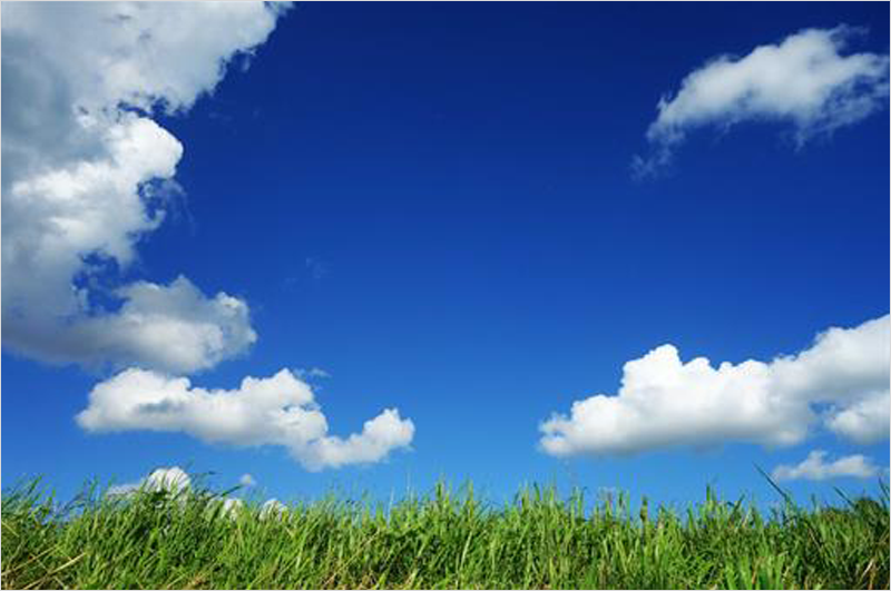 Césped verde y cielo azul con nubes blancas simulando aire limpio.