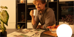 Chico sentado sonriendo y con una taza de café en la mano. Alrededor dos lámparas encendidas con luz tenue.