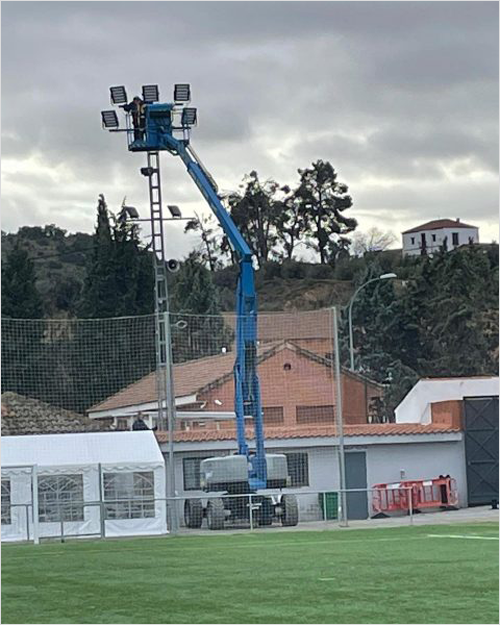 Operario cambiando las luces de un campo de fútbol subido a una grúa.