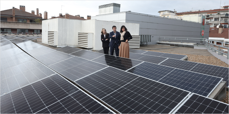 Placas solares instaladas en el tejado de un edificio y dos mujeres y un hombre visitando la instalación.