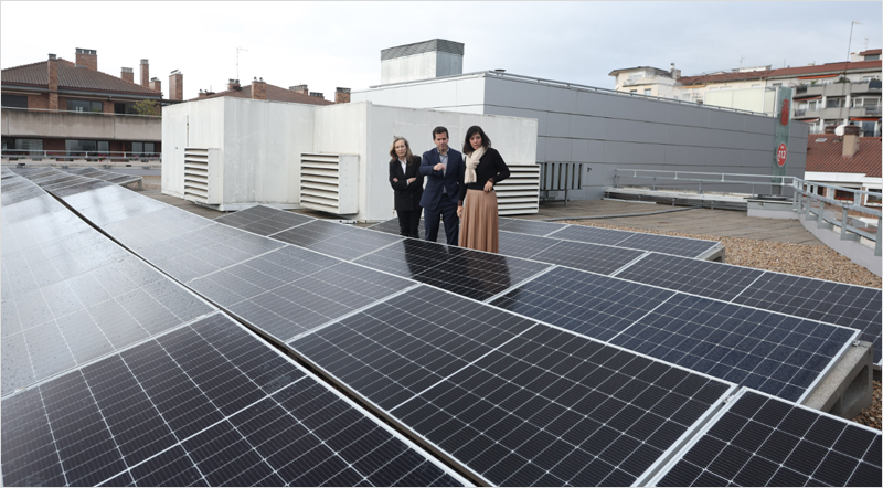 Placas solares instaladas en el tejado de un edificio y dos mujeres y un hombre visitando la instalación.