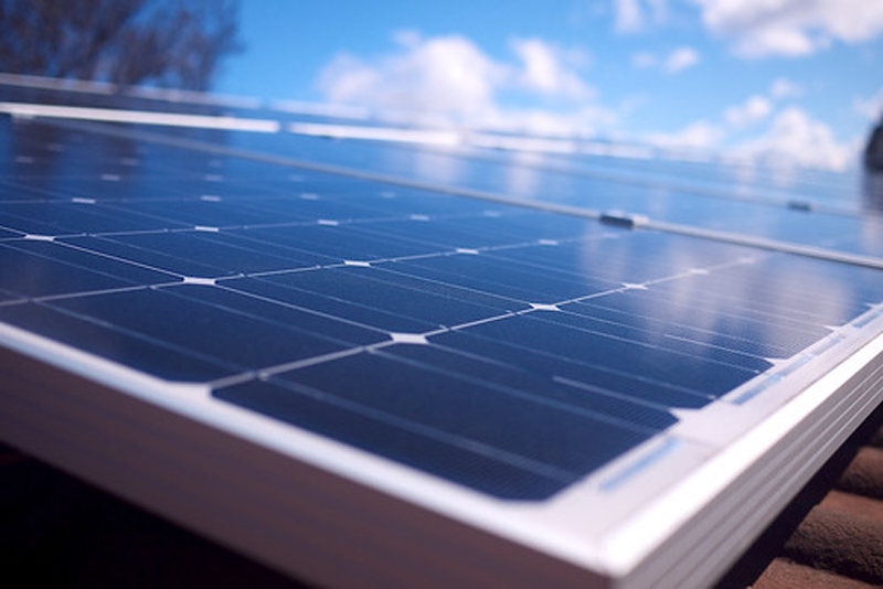 Placas solares instaladas en un tejado y un cielo azul con nubes al fondo.