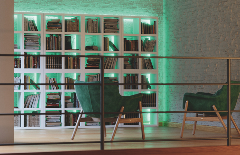 Estantería llena de libros iluminada con tonos verdes y dos butacas de color verde delante.