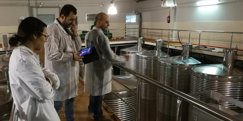 Proceso industrial de elaboración del vino y tres técnicos con bata blanca mirando el proceso.