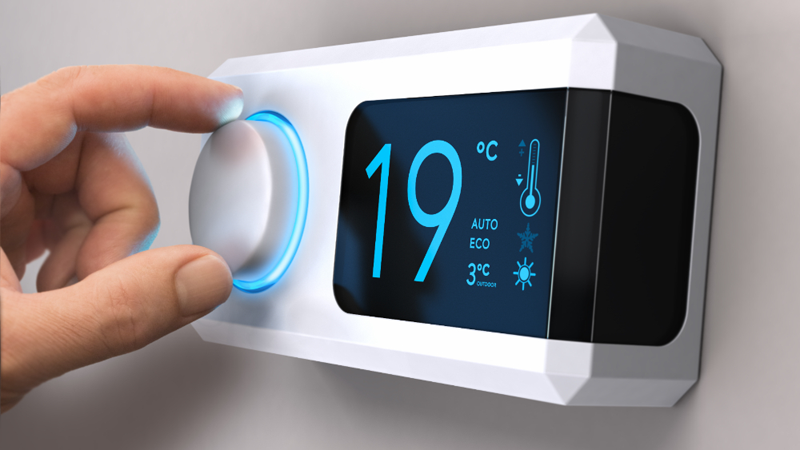 Una mano regulando un termostato que marca 19 grados.