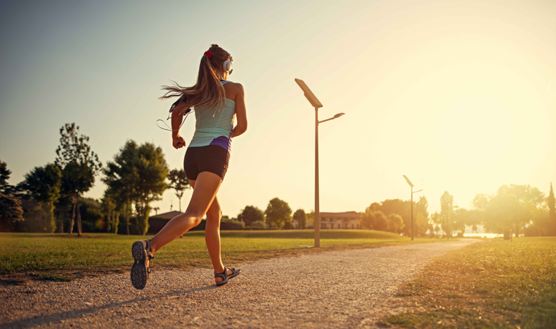 Mujer corriendo en un atardecer según cae el sol y unas farolas de iluminación solar en el recorrido.