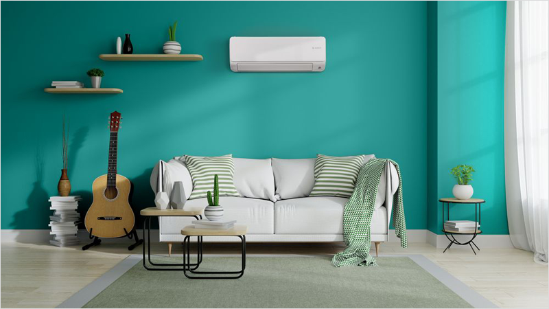 Sofá blanco en una salón luminoso con la pared en verde y un aparato de aire acondicionado instalado en la pared.