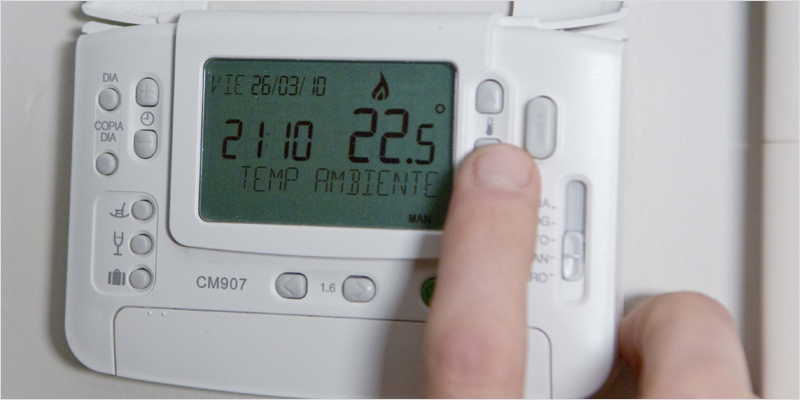 Dedo de un hombre tocando un botón de un termostato que marca 22,5 grados.