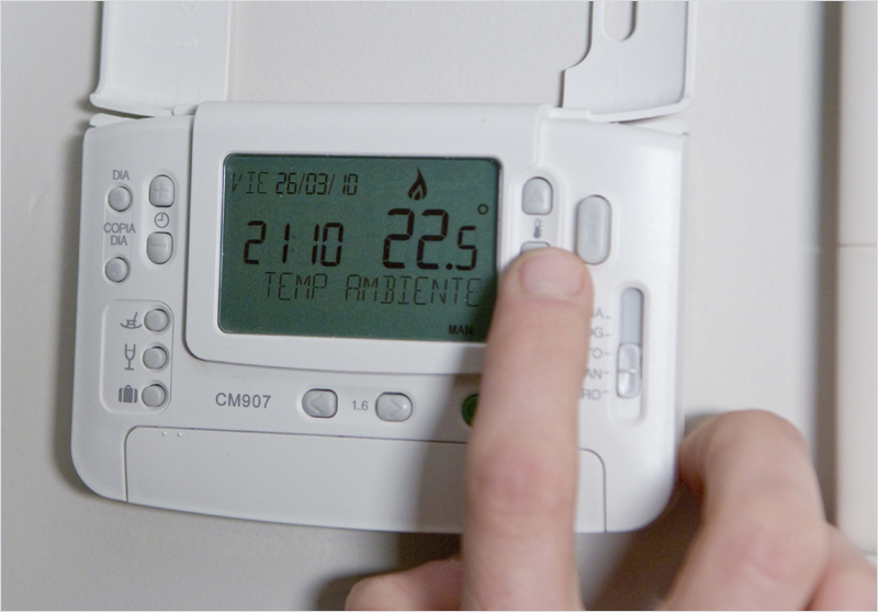 Dedo de un hombre tocando un botón de un termostato que marca 22,5 grados.