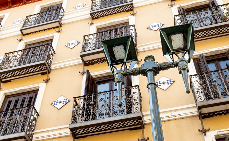 Farola con dos luminarias y detrás un edificio de viviendas.