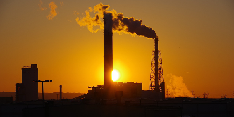 Fábrica echando humo en un atardecer de color naranja.