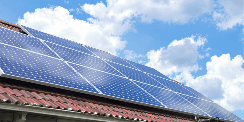Paneles solares instalados en el tejado de una casa, bajo un cielo azul con nubes blancas.